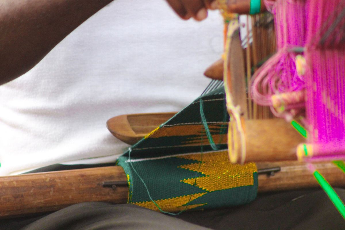 A close up image of kente cloth being woven on a person’s lap.