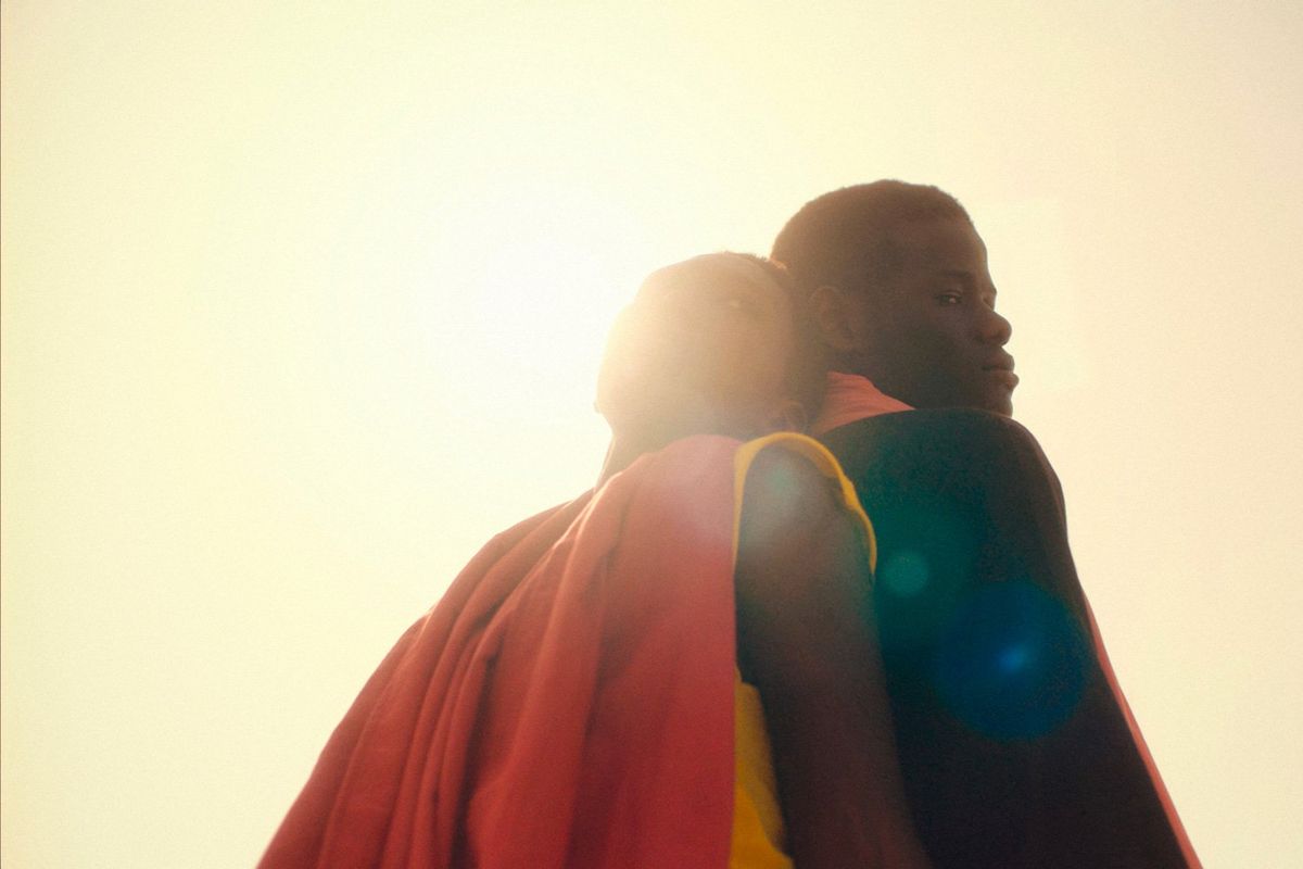 A still from the film, 'Banel & Adama' of two people, sitting back to back, with the sunlight peeking through their silhouette.